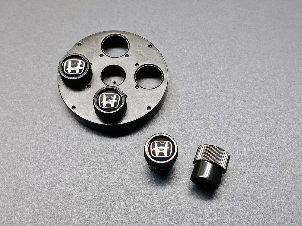 Close-up of OEM Honda black valve stem caps with silver H logo 08W48-PL4-100A