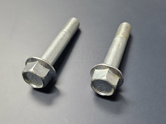 Two OEM Honda rear lower shock bolts laid flat on table – genuine factory hardware for Acura RSX DC5 2002–2006