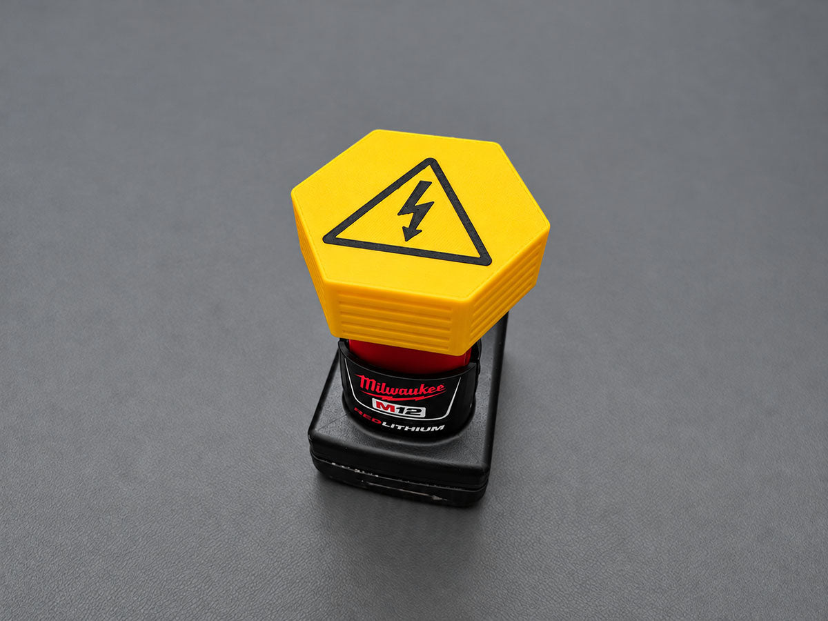 Yellow M12-compatible battery terminal cover with black electrical-warning graphic