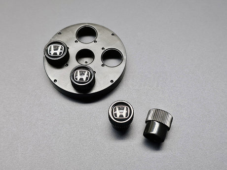 Close-up of OEM Honda black valve stem caps with silver H logo 08W48-PL4-100A