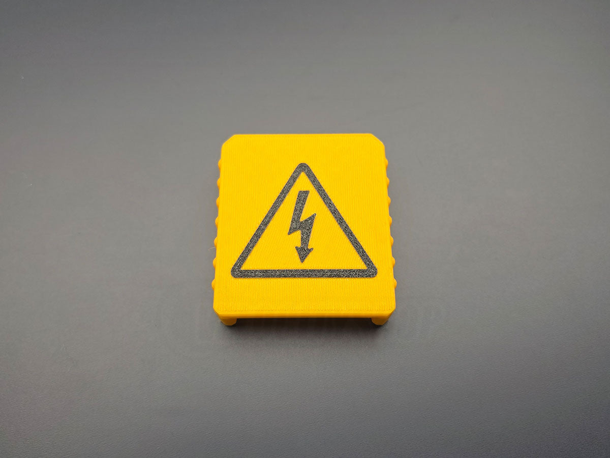 Yellow M18-compatible battery terminal cover with black electrical warning symbol