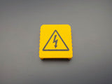 Yellow M18-compatible battery terminal cover with black electrical warning symbol