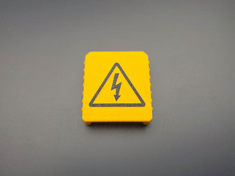 Yellow M18-compatible battery terminal cover with black electrical warning symbol